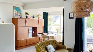 A living room with a wooden cabinet, a green armchair, and a woven pendant light. - "Chez Marinette" à Morgat - Maison & Jardin clos au calme, 6pers, plage à pied - (Crozon Morgat)