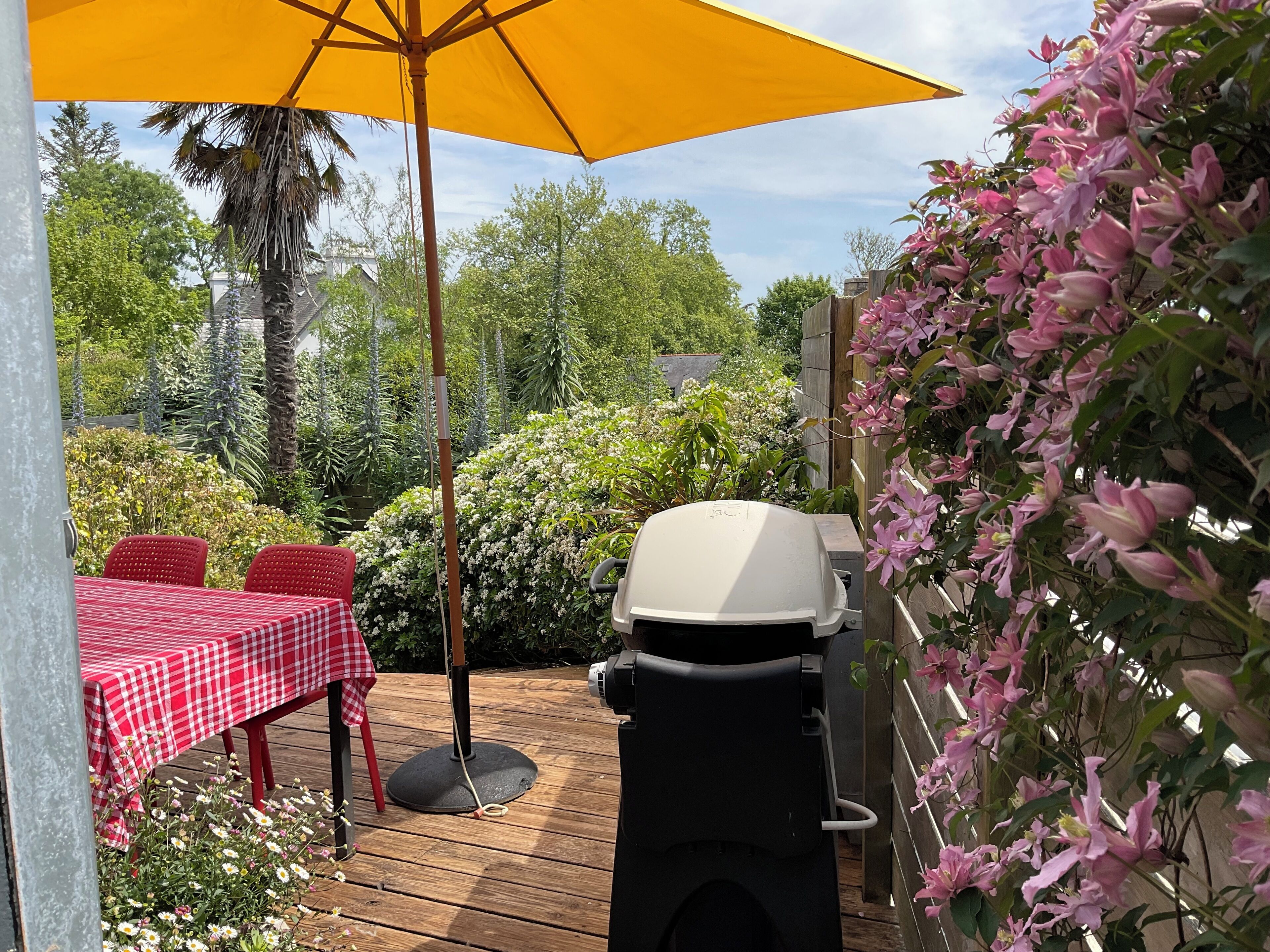 En terrasse med et rødt og hvidt skakternet bord, en gul parasol og en grill.