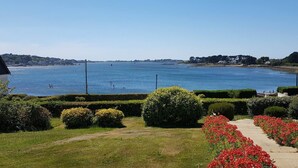 A waterfront property with a clear view of the sea, a well-maintained garden with red flowers, and a pathway leading to the water. - Grande Maison Avec vue Imprenable sur L'aber-wrac'h (Plouguerneau)