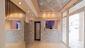 A modern reception area with a stone wall, wooden floor, and a glass door leading outside. - Azzuro Apartments (Budva)