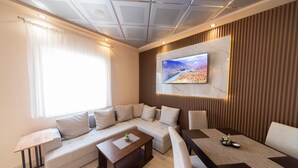 A modern living room with a sectional sofa, a coffee table, and a TV mounted on a wooden panel wall. - Azzuro Apartments (Budva)