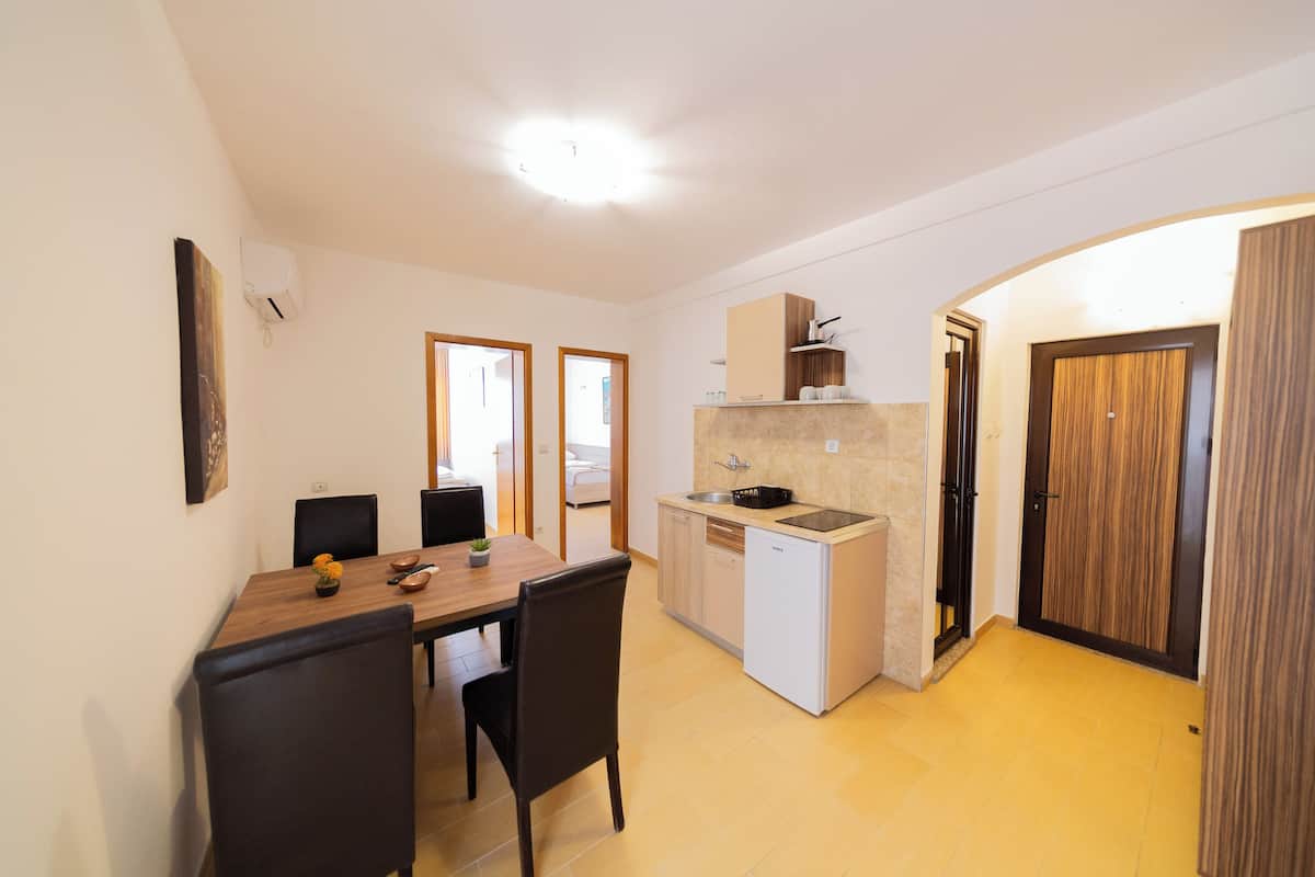Cocina compacta con zona de comedor, un refrigerador pequeño y un microondas. Hay dos sillas en la mesa de comedor y una pequeña planta en maceta sobre la mesa.