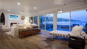 Ein modernes Wohnzimmer mit einem großen Schiebeglasfenster, das auf eine Terrasse im Freien führt, einem weißen Kamin und Blick aufs Meer.