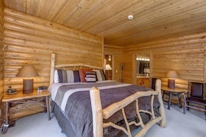 Un dormitorio tipo cabaña de madera con una cama de madera, lámparas de noche, un espejo y una mesita.