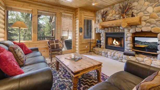 A log cabin interior with a stone fireplace, leather sofas, and a large window. - Abode at Black Bear #253, hot tub, pool & gym, Deer Valley (Park City)
