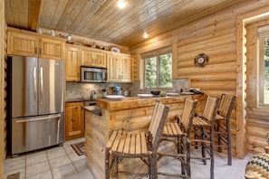 Cocina de cabaña de madera con armarios de madera, un refrigerador de acero inoxidable, un microondas y una mesa de comedor de madera con sillas.