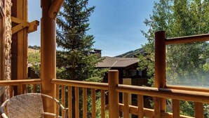 A wooden balcony with a wicker chair, overlooking a mountainous landscape with trees and buildings. - Abode at Black Bear #353, private hot tub, pool, Deer Valley (Park City)