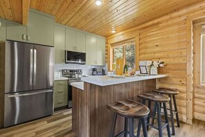 A modern kitchen with stainless steel appliances, a central island with stools, and wooden paneling.