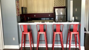 Une cuisine avec trois tabourets de bar rouges, un réfrigérateur en acier inoxydable et des meubles de couleur claire.