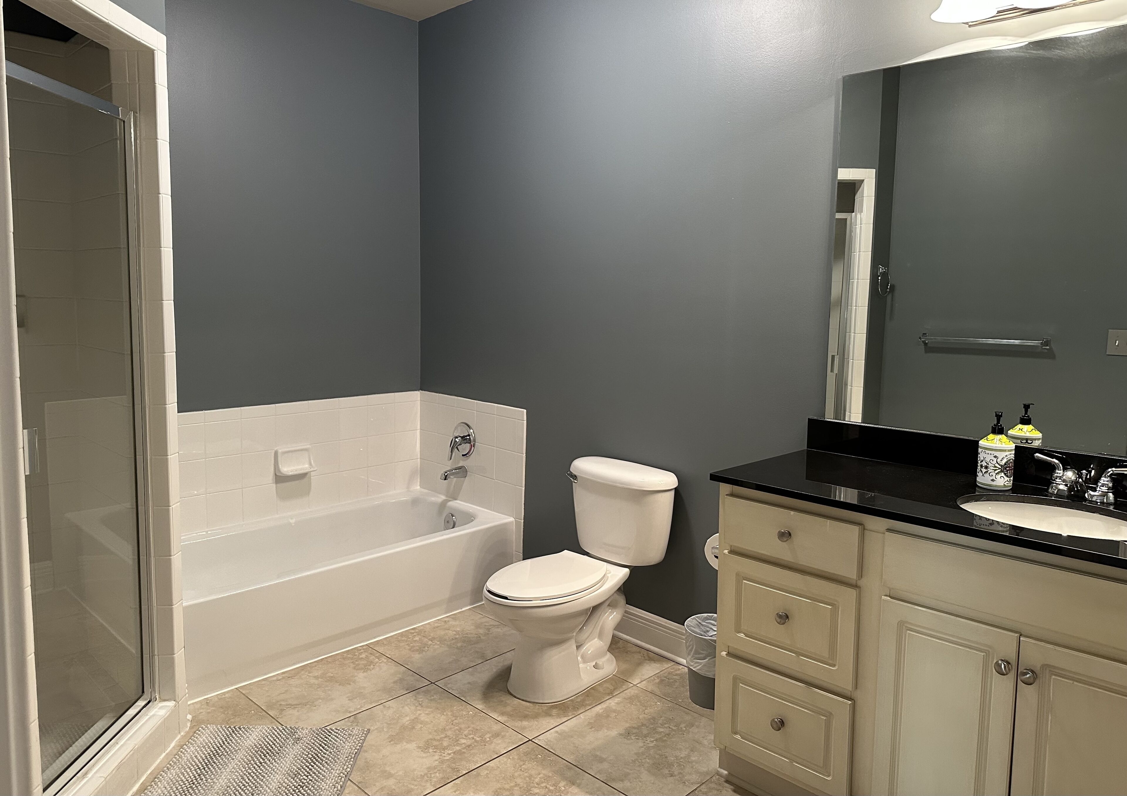 A bathroom with a bathtub, toilet, vanity, and a large mirror.