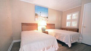 A room with two beds, a nightstand with a lamp, a painting on the wall, and a window with blinds. - Relax in this 2 BD/2Bath Direct Ocean Front. Listen to the ocean waves and enjoy. (OCEAN CITY)