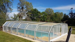 Una estructura de invernadero con piscina, rodeada de césped y árboles.