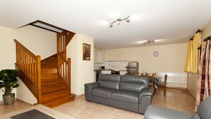Una sala de estar con un sofá de cuero gris, una escalera de madera y una cocina al fondo.