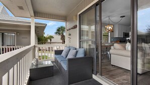 A covered balcony with a sofa and table, sliding glass doors leading to a kitchen area. - Beachy, Modern & Updated - Seagrove Beach on 30A + Free Attraction Tickets! (Santa Rosa Beach)