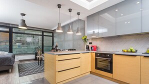 Une cuisine moderne dotée d’un îlot central, d’un four encastré et de luminaires suspendus.