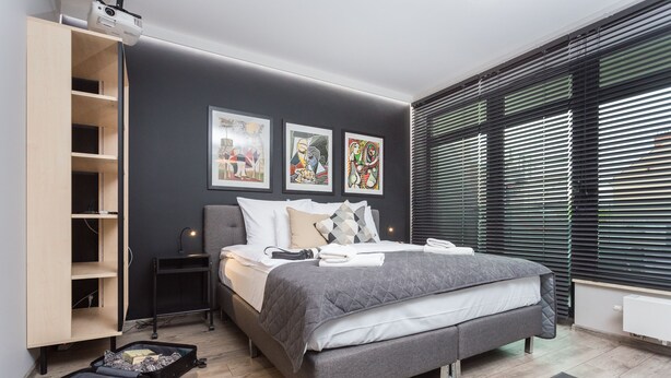 Une chambre moderne avec un lit gris, une armoire en bois et un projecteur fixé au plafond.