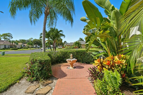 A garden pathway with a fountain, palm trees, and tropical plants.