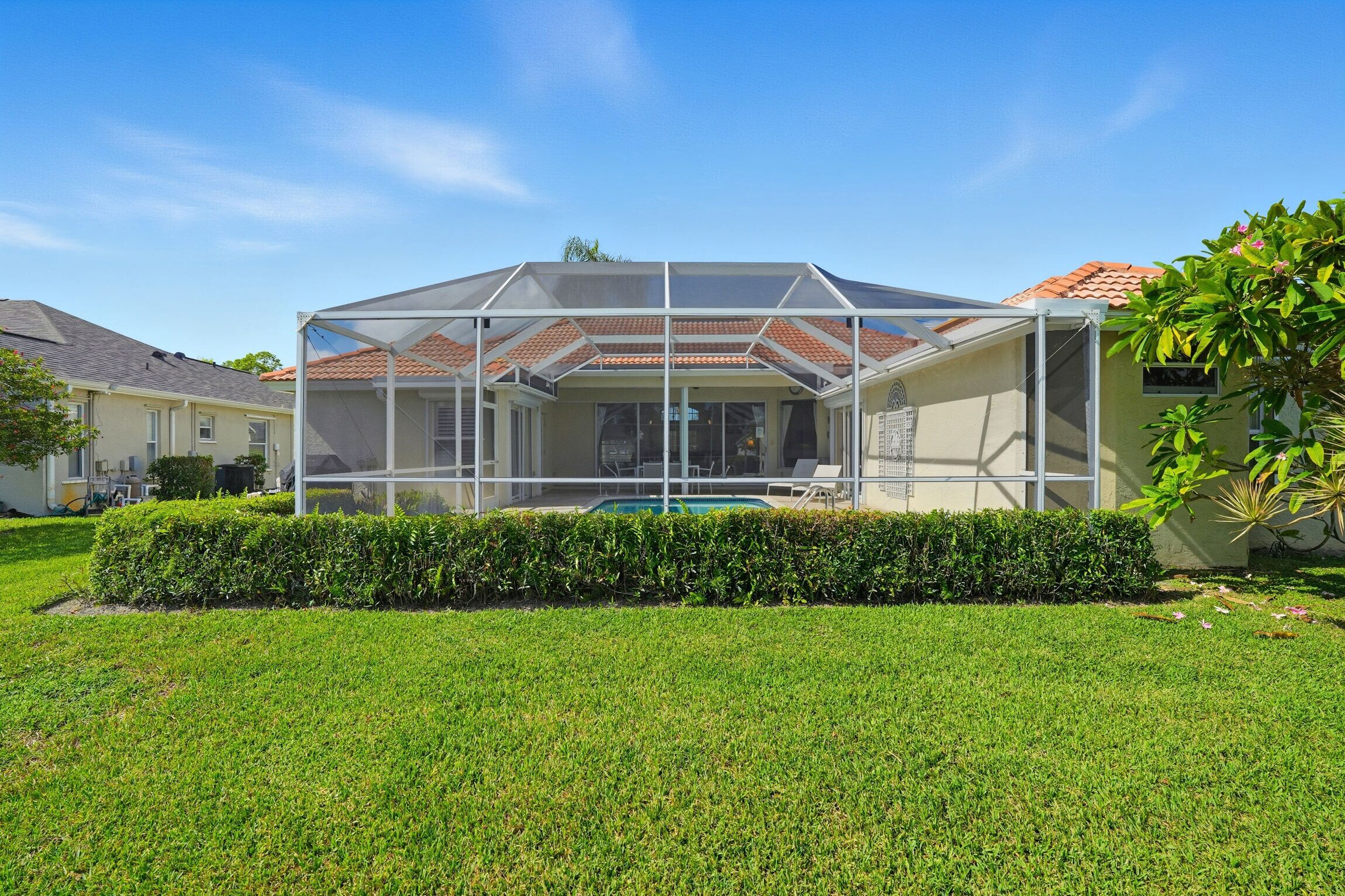 A house with a covered patio, a swimming pool, and a well-maintained lawn.