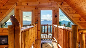 Une cabane en bois avec un balcon, un tableau représentant un cerf, et une vue sur les montagnes.