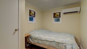A small bedroom with a single bed, two windows, and an air conditioning unit.