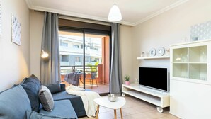 Een moderne woonkamer met een bank, televisie en een balkon met gordijnen.