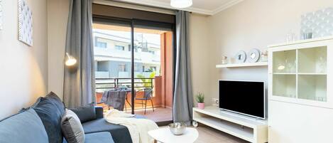 Una sala moderna con sofá, televisor y un balcón con cortinas.