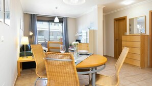 Een eethoek met een ronde tafel, rieten stoelen, een kroonluchter en uitzicht op het buiten.
