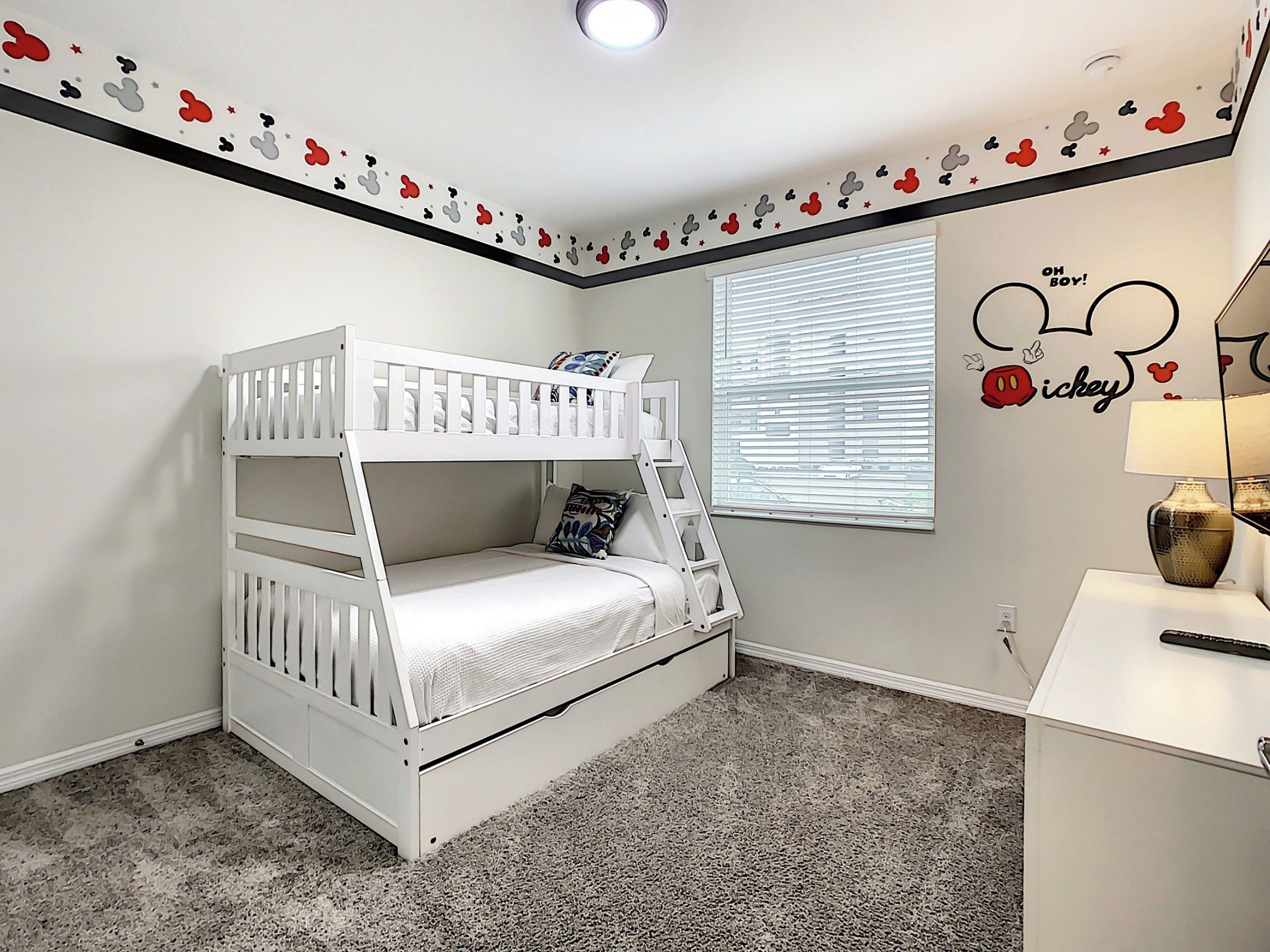 A bunk bed in a room with a Mickey Mouse wall decal and a window with blinds.