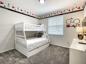 Ein Etagenbett in einem Zimmer mit einer Wandsticker-Motivierung von Mickey Mouse und einem Fenster mit Jalousien.