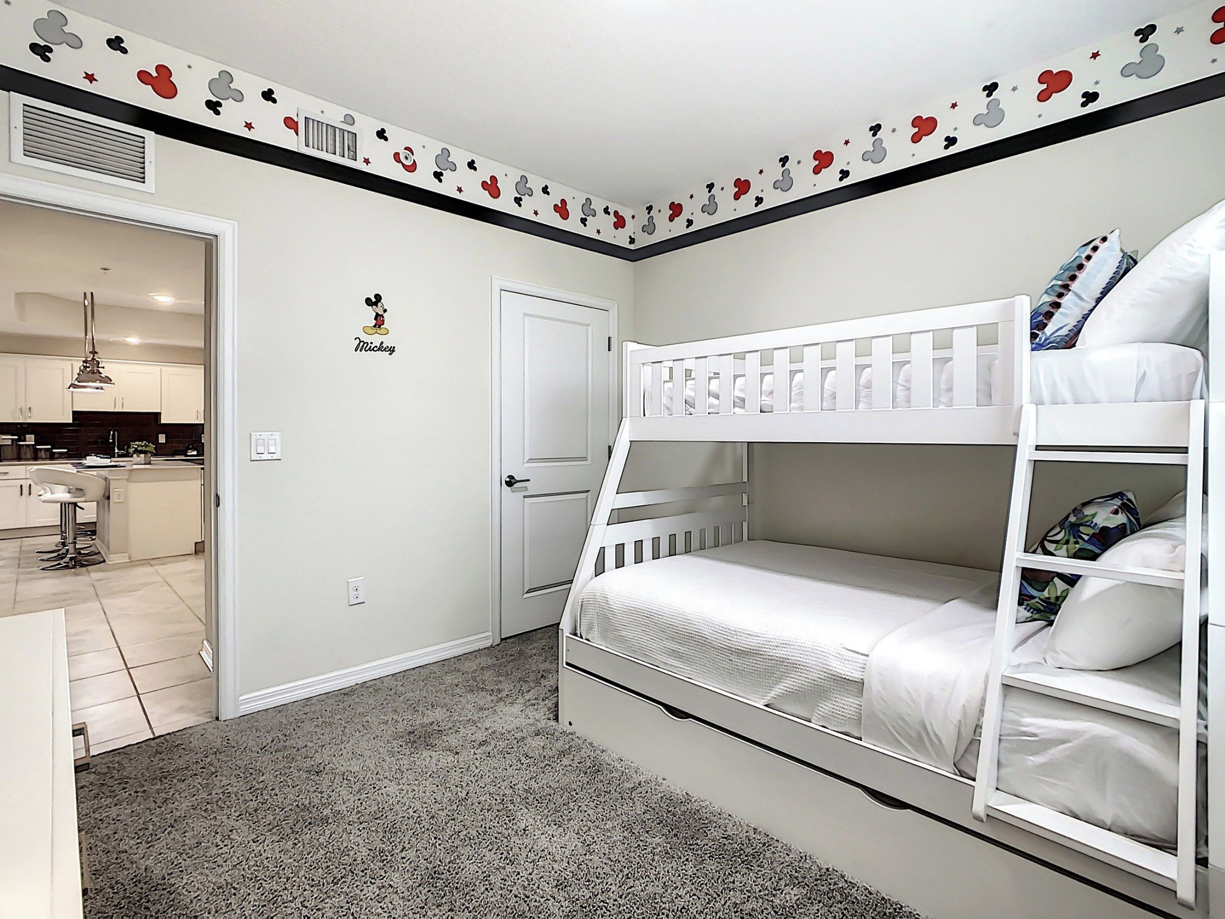 A child's bedroom with bunk beds, a Mickey Mouse decal, and a kitchen in the background.