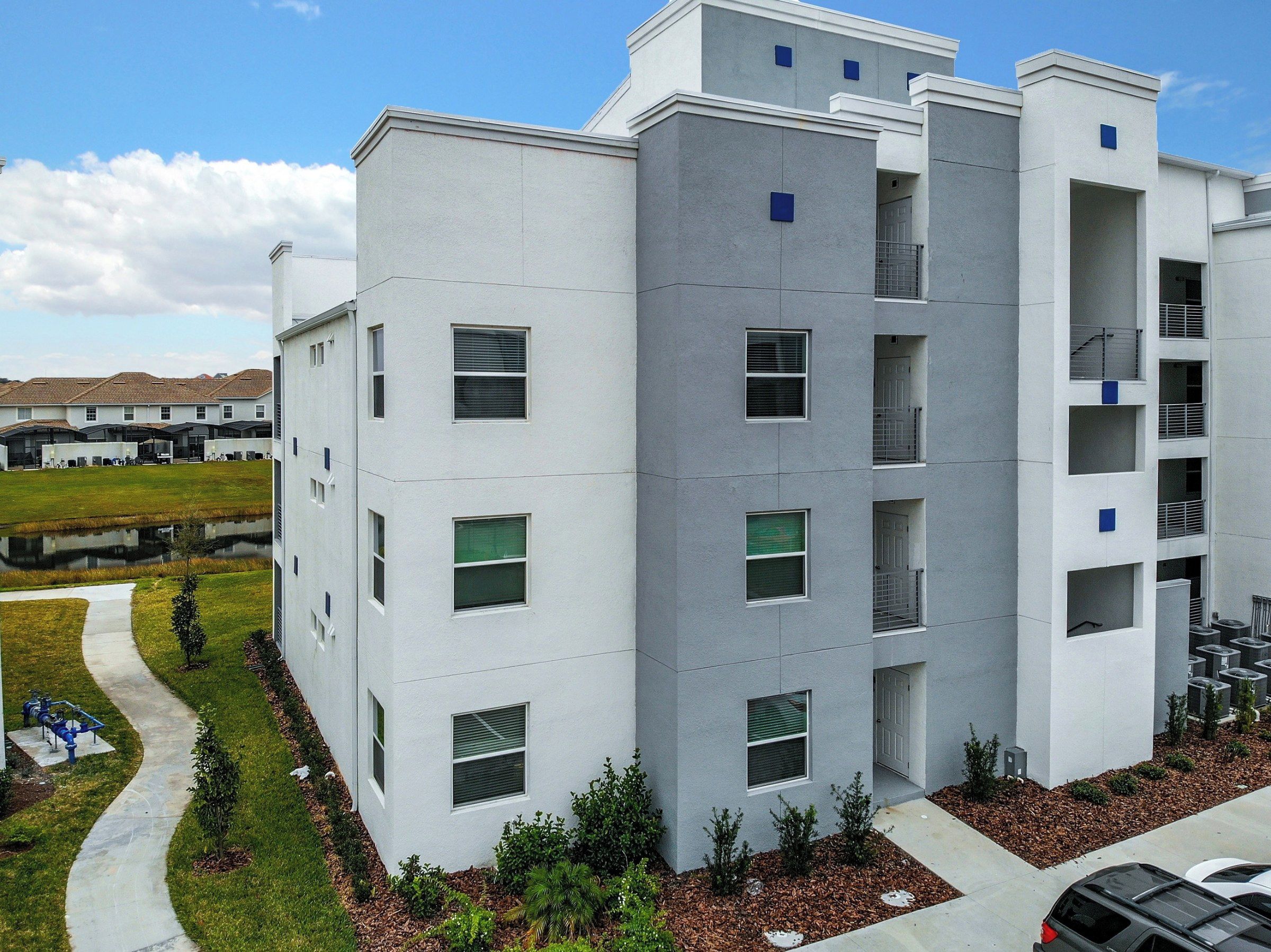 A multi-story residential building with balconies, a covered outdoor area, and a pathway leading to the entrance.