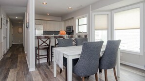 A modern kitchen with white cabinets, a central island, and a dining area with grey chairs. - Stunning 3 Bedroom Condo Near Crystal Pier (Wrightsville Beach)