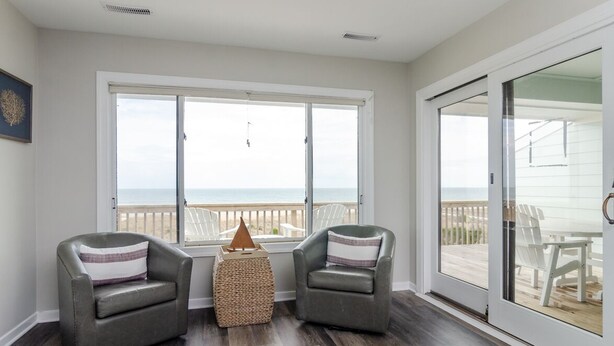 A room with two leather armchairs, a woven ottoman, and a large window overlooking a deck with outdoor furniture. - Stunning 3 Bedroom Condo Near Crystal Pier (Wrightsville Beach)