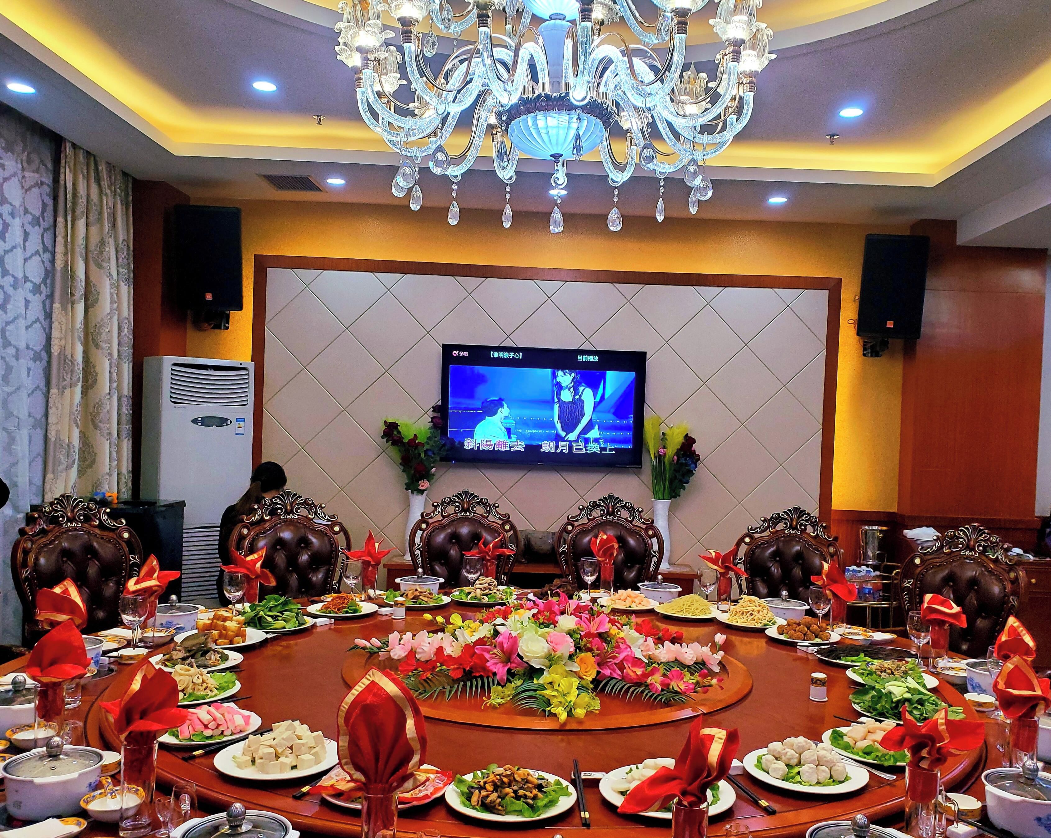 A conference room with a large round table, chairs, a television screen, and a chandelier.