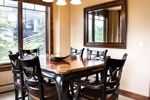 Une salle à manger avec une table et des chaises en bois, une grande fenêtre et un miroir au mur.