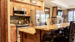 Una cocina con armarios de madera, electrodomésticos de acero inoxidable, encimera de granito y una isla integrada con asientos tipo barra.