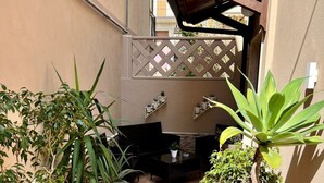 Un pequeño patio con plantas en macetas, piso de baldosas y una estructura de pérgola de madera.