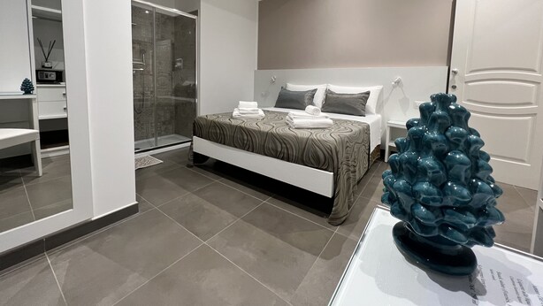 Un dormitorio moderno con una cama, mesita de noche y un jarrón decorativo.