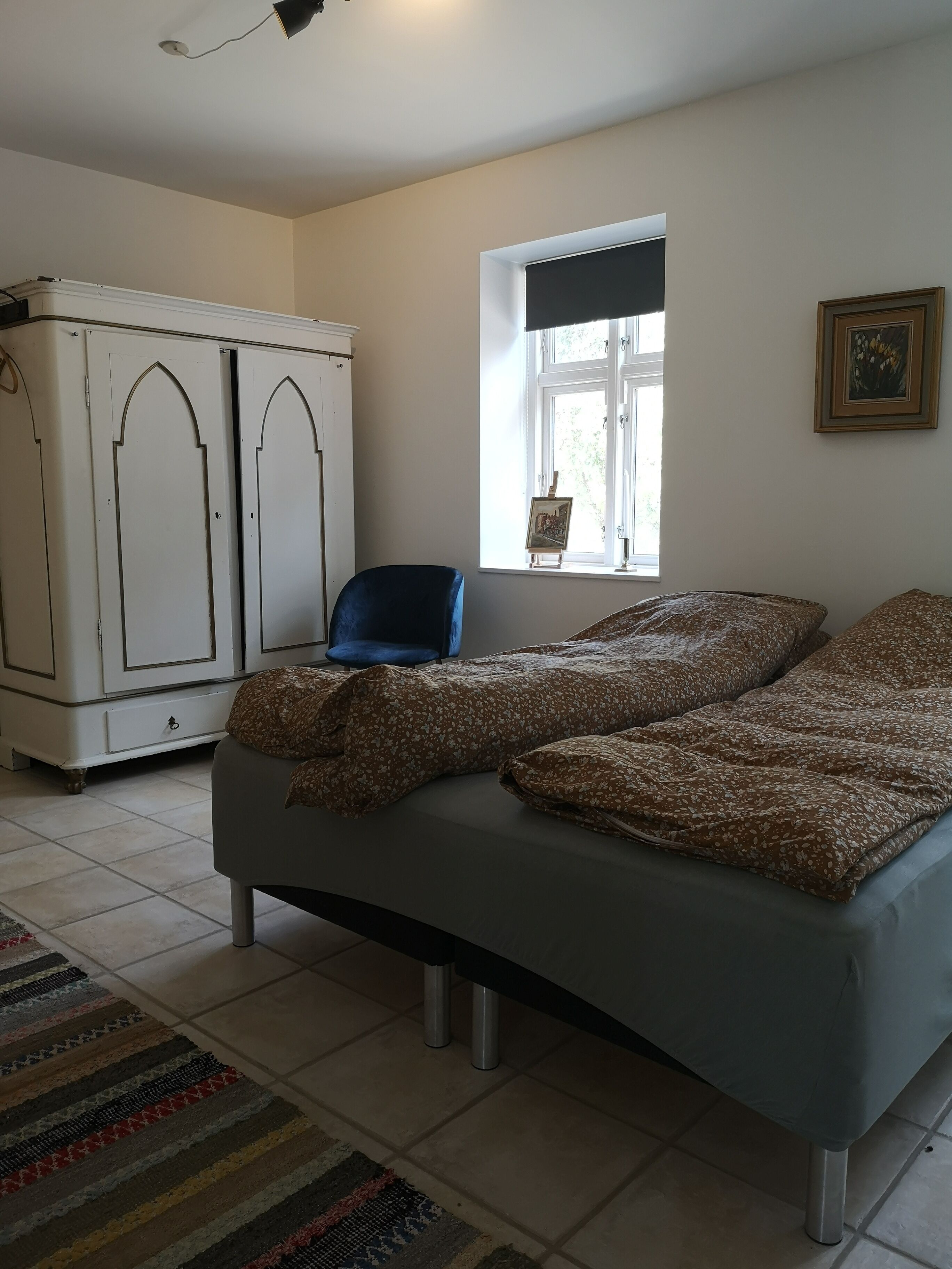A bedroom with a bed, a wardrobe, a chair, a window, and a rug.