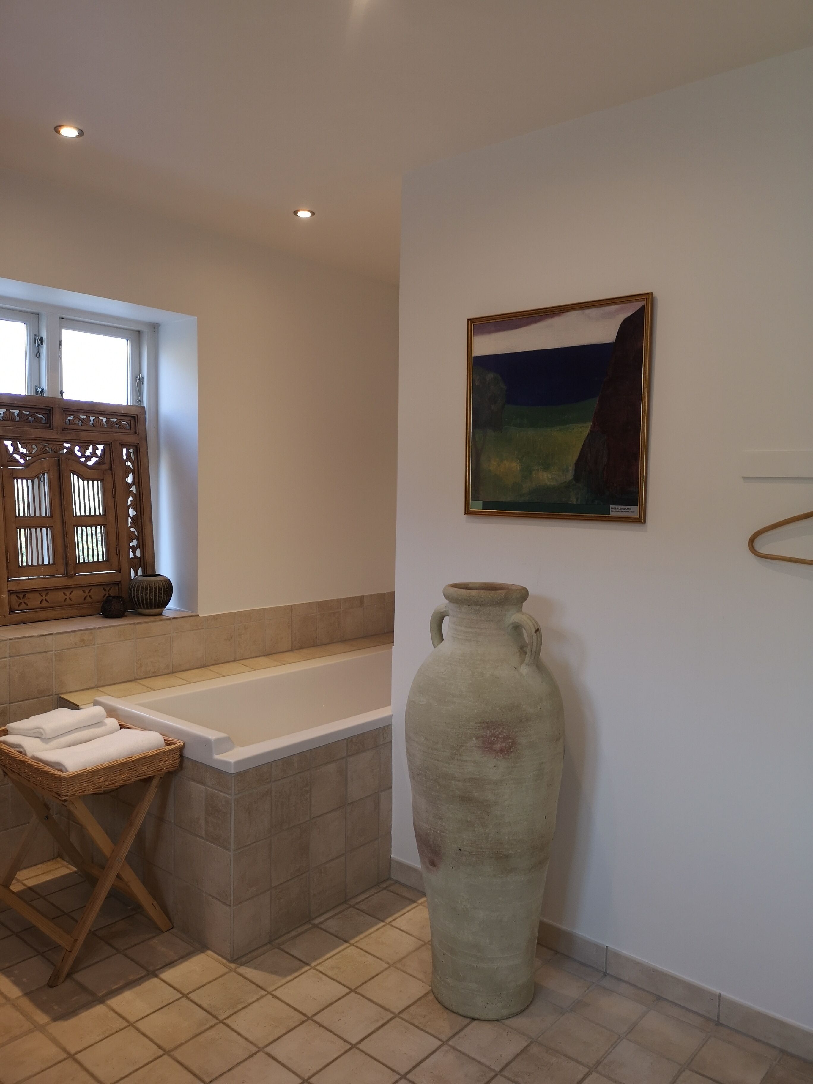A bathroom with a bathtub, a large vase, and a painting on the wall.