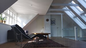 A spacious loft bedroom with a sloped ceiling, skylights, a large window, and a black chair. - MidtGolf Guest house (Regstrup)