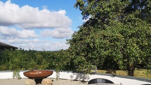 An outdoor patio with wicker furniture, a large metal bowl, and a tree with green leaves. - MidtGolf Guest house (Regstrup)