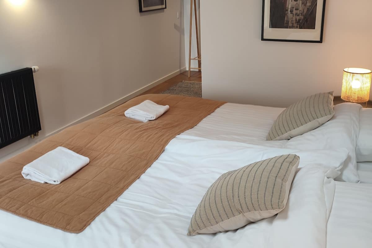 Ett hotellrum med två sängar, ett trägolv, ett element, en golvlampa och en inramad tavla på väggen.