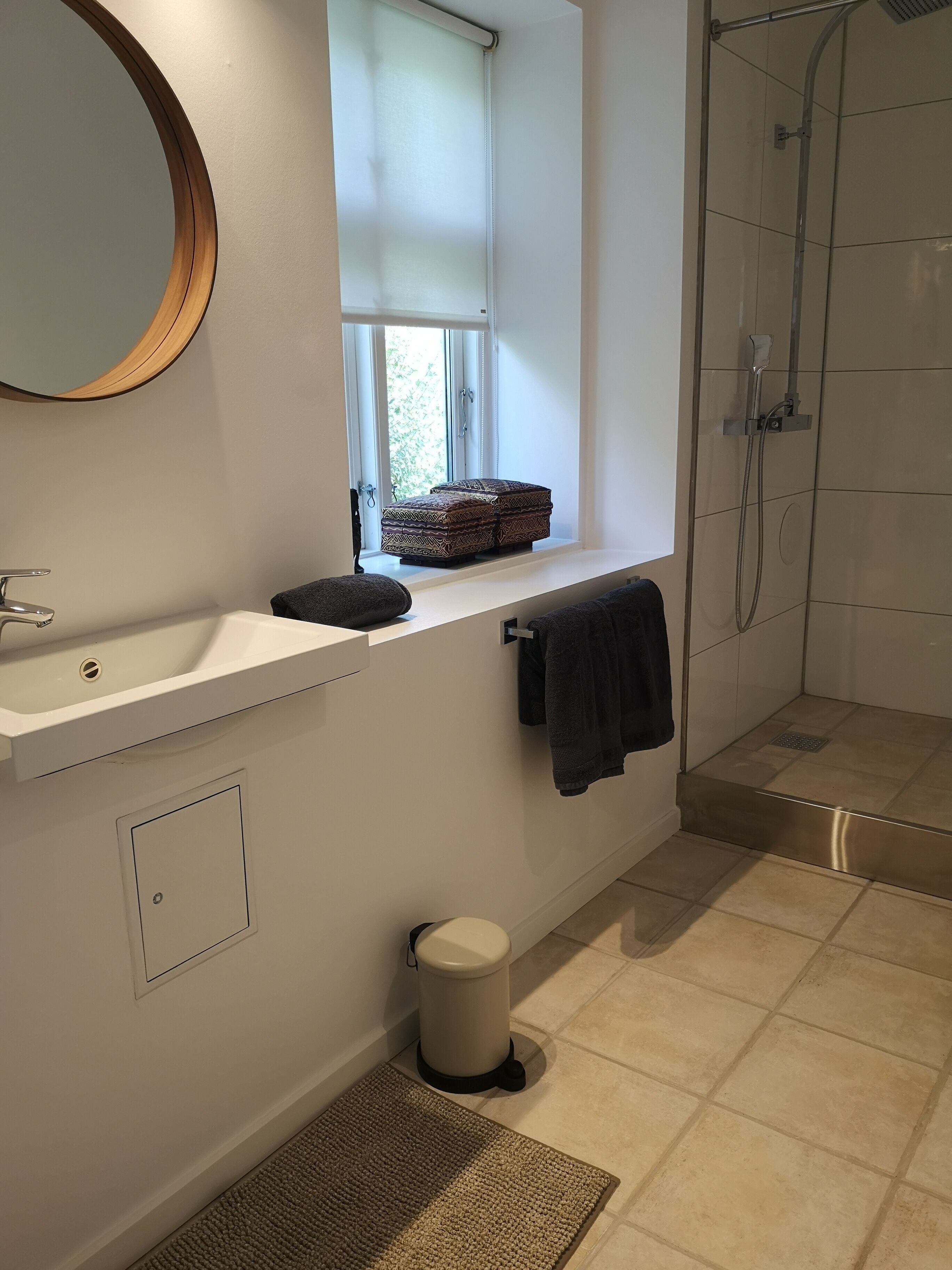 Ein Badezimmer mit Fenster, Waschbecken, Handtuchhalter, Dusche und Toilette.