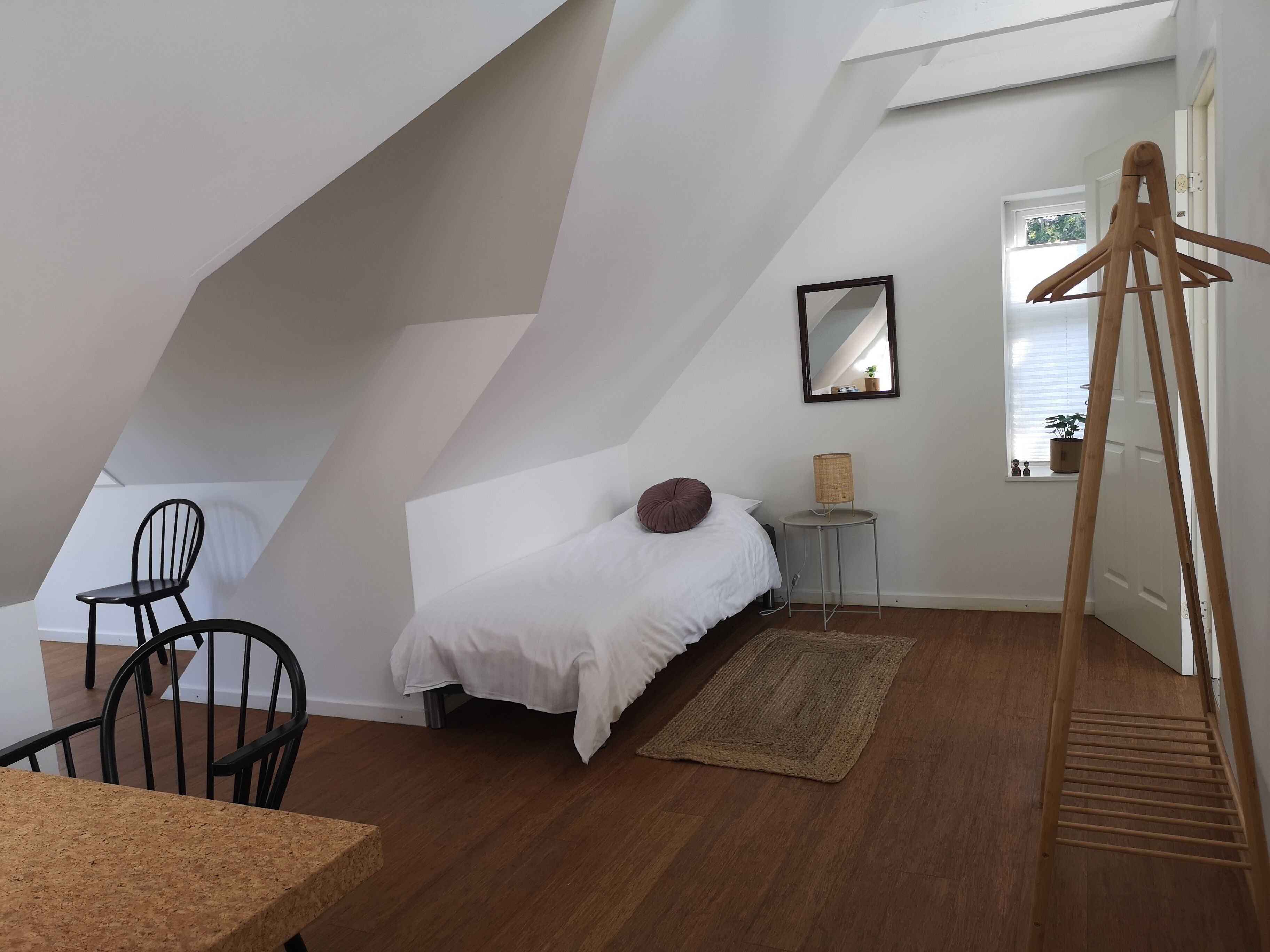 A bedroom with a bed, a chair, a small table, a lamp, and a window with a view of the outside.