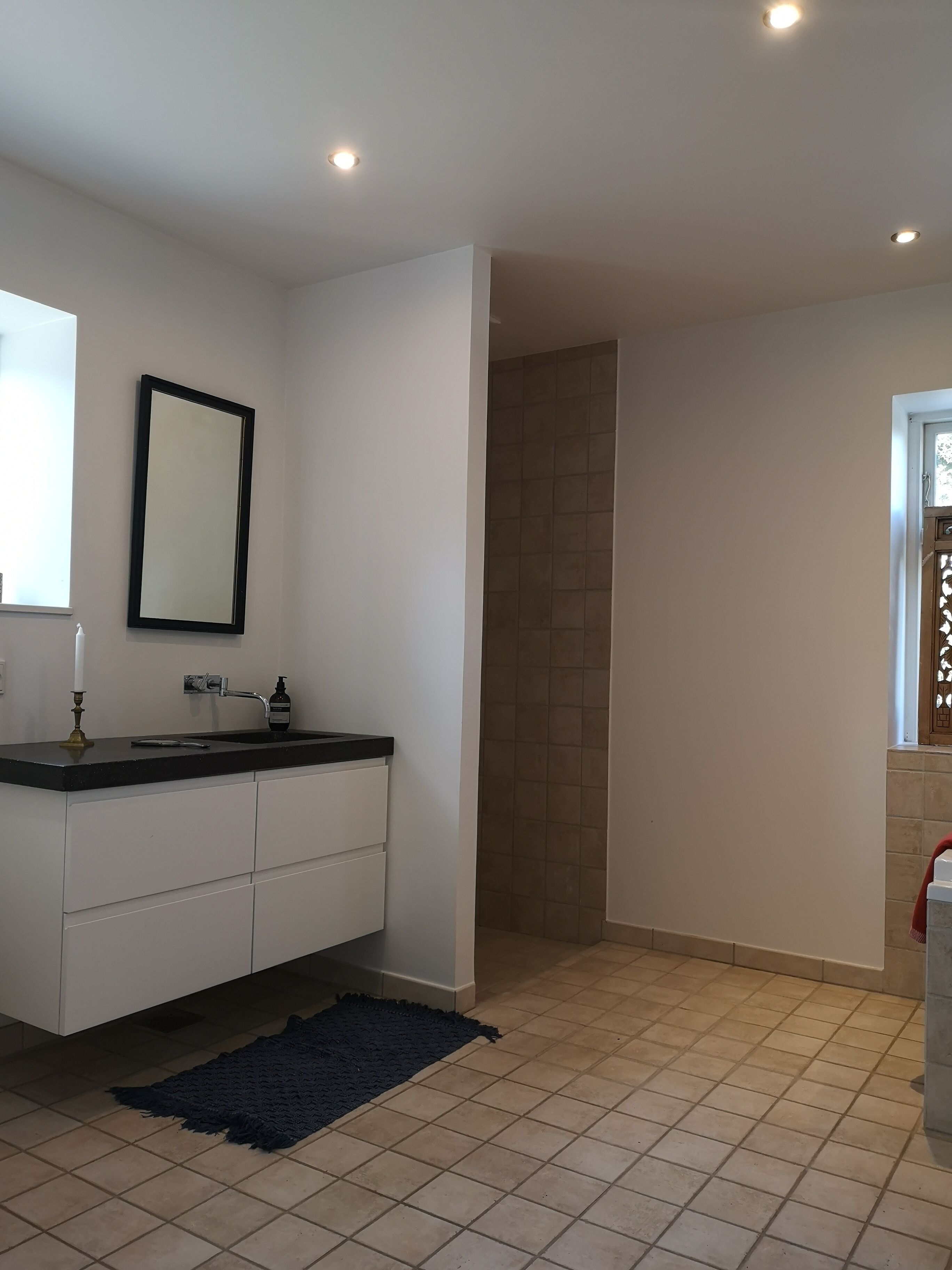 Un baño moderno con lavamanos de superficie negra, armarios blancos, alfombra azul oscuro y suelo de baldosas.