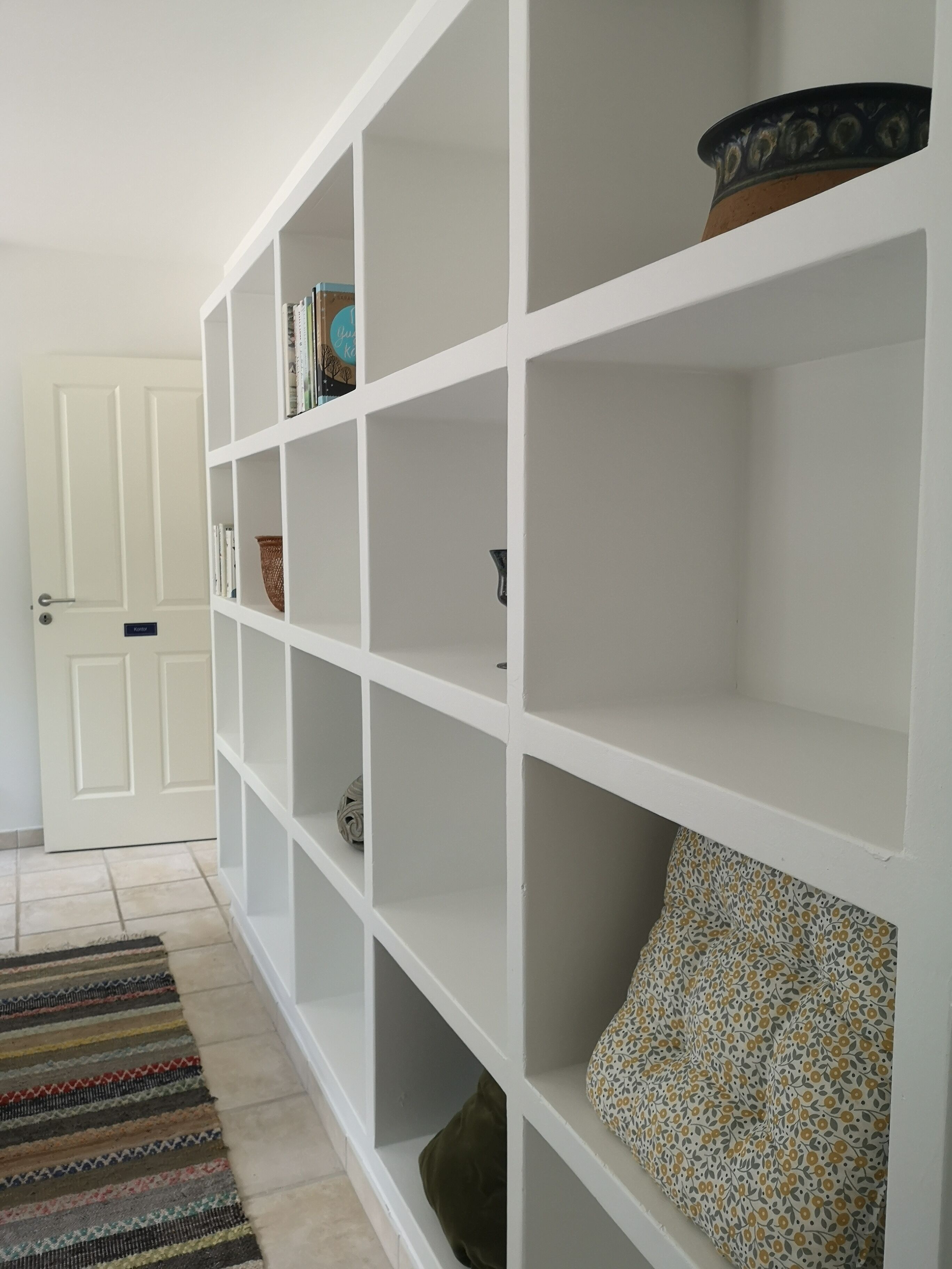 A hallway with a white shelving unit, a patterned rug, and a door.
