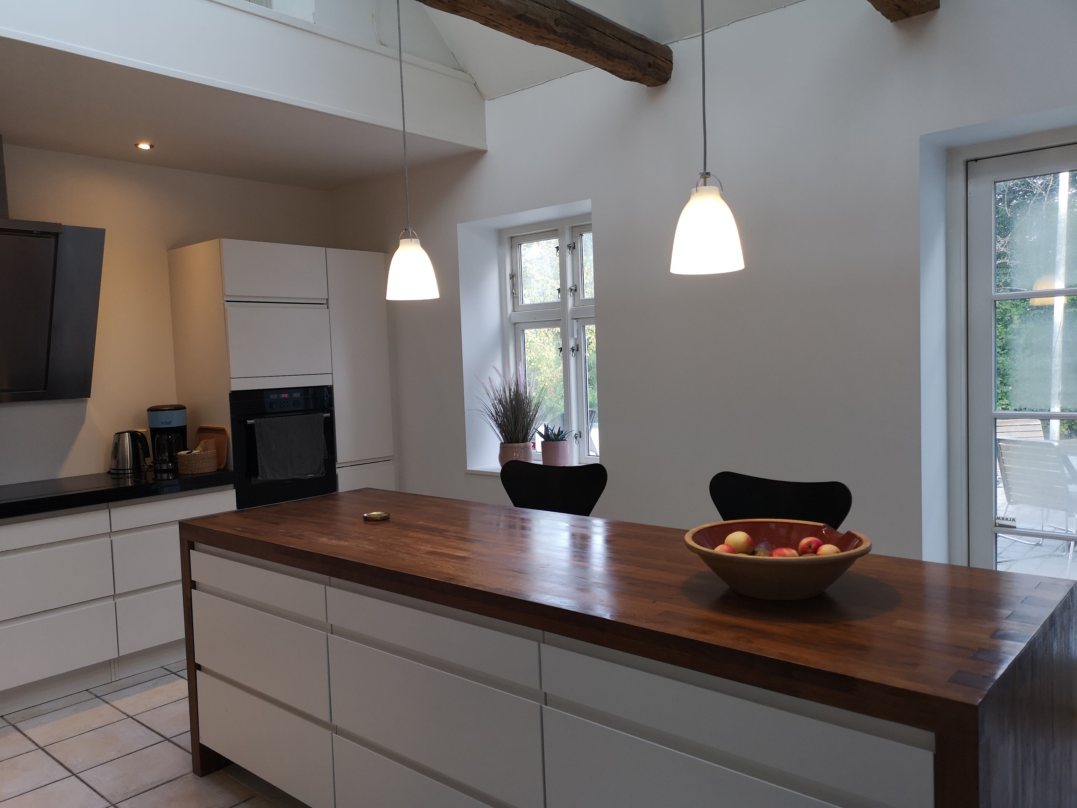 Una cocina moderna con armarios blancos, una isla de madera, iluminación colgante y vistas al exterior.