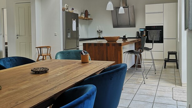 A modern kitchen with a wooden ceiling, a dining area with blue chairs, and a kitchen island. - MidtGolf Guest house (Regstrup)
