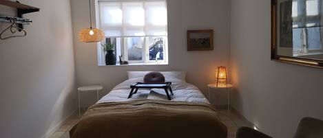 Un dormitorio con cama, lámparas de noche, una ventana y una silla.